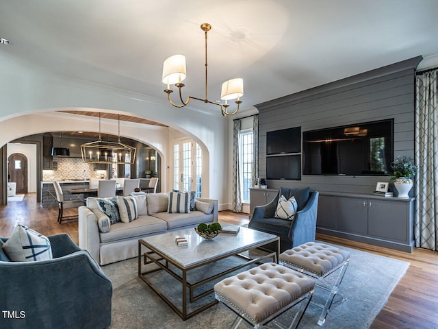 living area featuring arched walkways, a chandelier, and wood finished floors