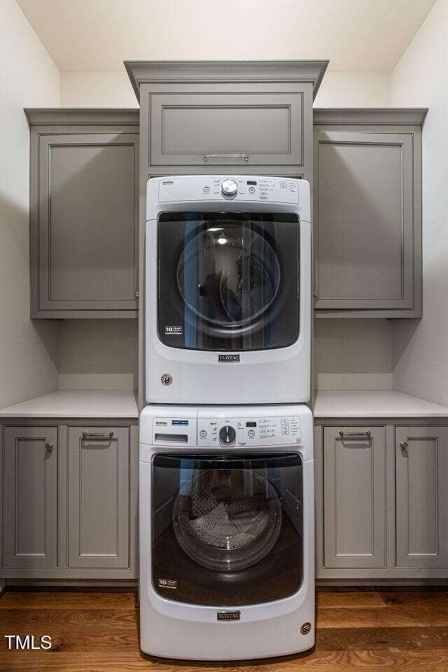 laundry room featuring stacked washer and dryer, cabinet space, and wood finished floors