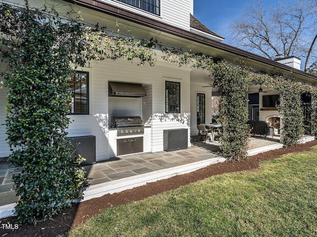 view of patio with ceiling fan, an outdoor kitchen, a grill, and a fireplace