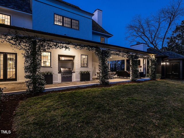 back of property featuring a chimney, a lawn, and a patio