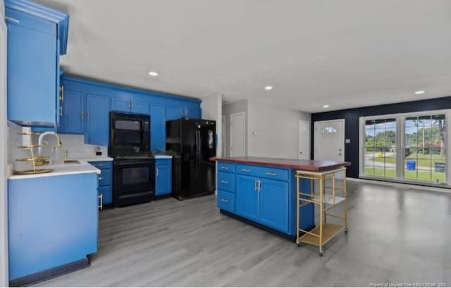 kitchen featuring sink, light wood-type flooring, black appliances, and blue cabinetry