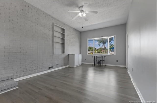 unfurnished living room with dark wood-type flooring, ceiling fan, brick wall, and a textured ceiling