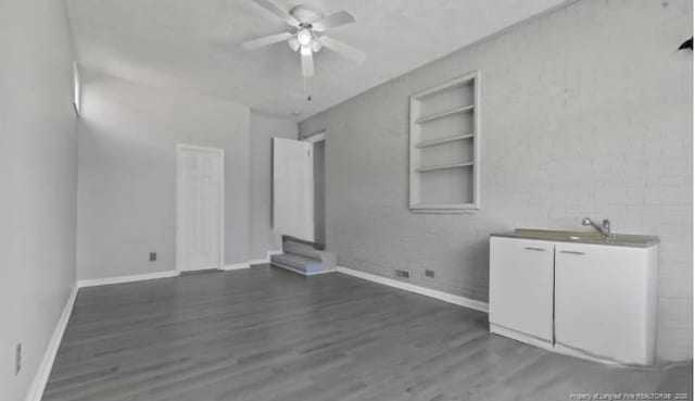 interior space with dark hardwood / wood-style flooring, built in features, ceiling fan, and brick wall