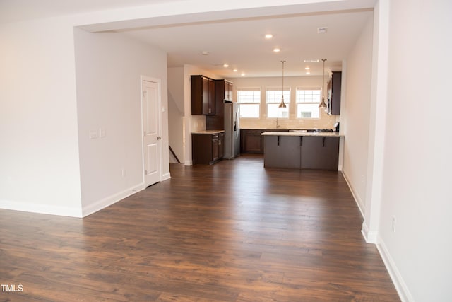 kitchen with dark hardwood / wood-style floors, pendant lighting, stainless steel fridge, decorative backsplash, and dark brown cabinets