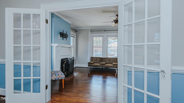 interior space with a brick fireplace, ceiling fan, ornamental molding, and dark wood-style flooring