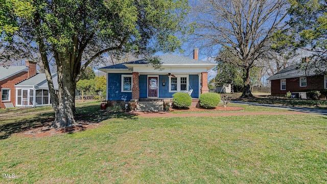 bungalow-style house with covered porch, a chimney, a front yard, and a ceiling fan