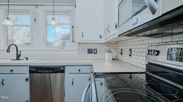 kitchen with stainless steel appliances, a sink, light countertops, tasteful backsplash, and pendant lighting