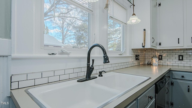 kitchen featuring decorative backsplash, dishwashing machine, decorative light fixtures, light countertops, and a sink