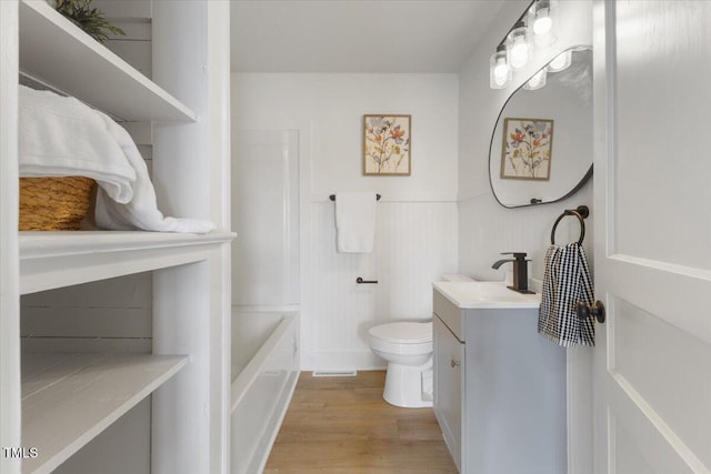 bathroom with hardwood / wood-style flooring, a tub to relax in, vanity, and toilet