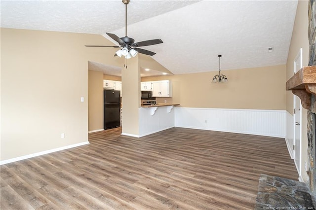 unfurnished living room with lofted ceiling, a stone fireplace, a textured ceiling, dark hardwood / wood-style flooring, and ceiling fan with notable chandelier