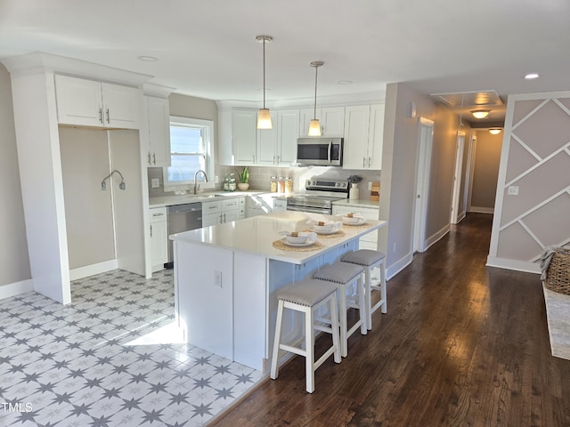 kitchen with sink, white cabinetry, appliances with stainless steel finishes, a kitchen island, and pendant lighting