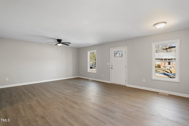 empty room with dark hardwood / wood-style floors, a wealth of natural light, and ceiling fan