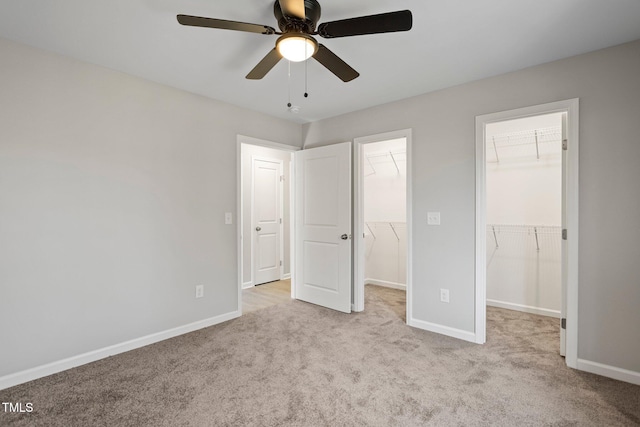 unfurnished bedroom featuring ceiling fan, a walk in closet, a closet, and light carpet