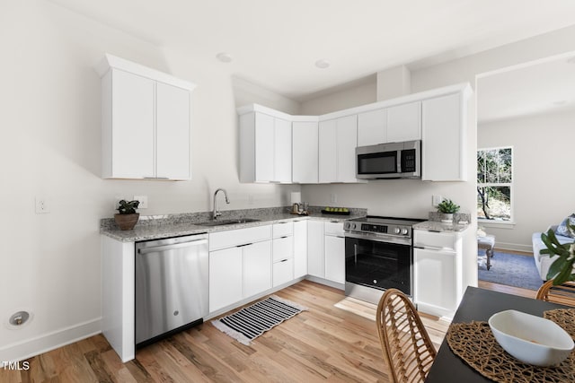 kitchen with white cabinetry, sink, light stone counters, stainless steel appliances, and light hardwood / wood-style flooring