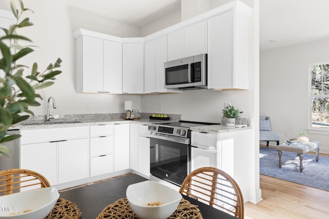 kitchen with sink, appliances with stainless steel finishes, light stone counters, white cabinets, and light wood-type flooring