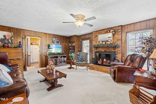 carpeted living room featuring ceiling fan, a brick fireplace, a textured ceiling, and wooden walls