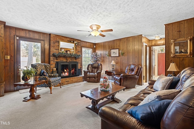 carpeted living room featuring a brick fireplace, a textured ceiling, wooden walls, and ceiling fan