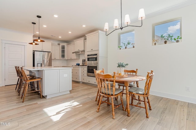 dining space with ornamental molding and light hardwood / wood-style flooring