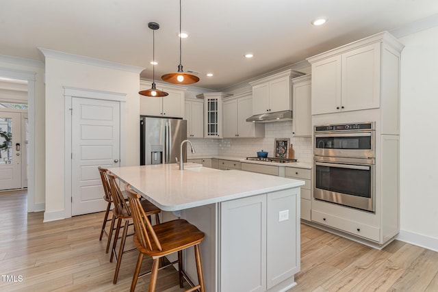 kitchen with pendant lighting, sink, backsplash, a kitchen island with sink, and stainless steel appliances