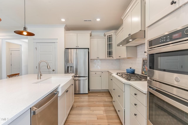 kitchen featuring pendant lighting, sink, backsplash, stainless steel appliances, and light hardwood / wood-style floors