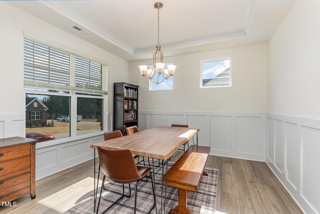 dining space with an inviting chandelier, a raised ceiling, and light hardwood / wood-style floors