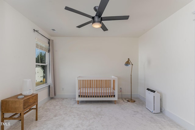 carpeted bedroom featuring a nursery area and ceiling fan