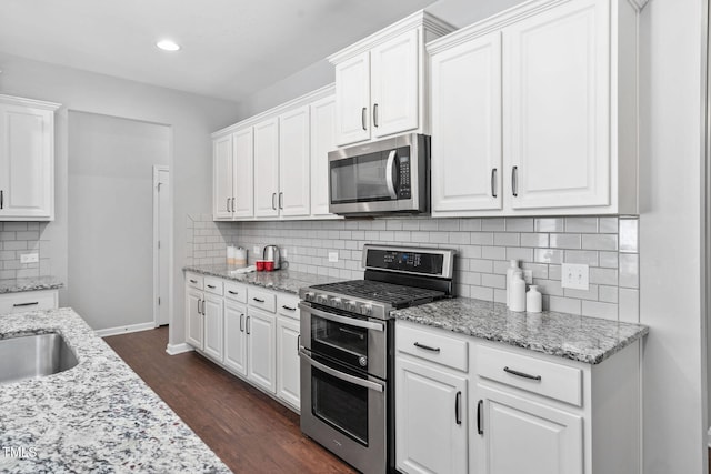 kitchen featuring light stone counters, dark wood-type flooring, stainless steel appliances, white cabinetry, and backsplash