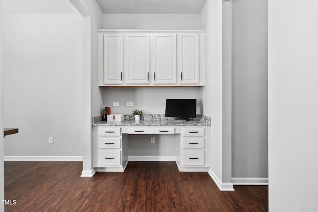 unfurnished office featuring dark wood finished floors, built in desk, and baseboards