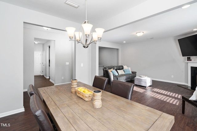 dining space with a fireplace with raised hearth, a chandelier, wood finished floors, visible vents, and baseboards