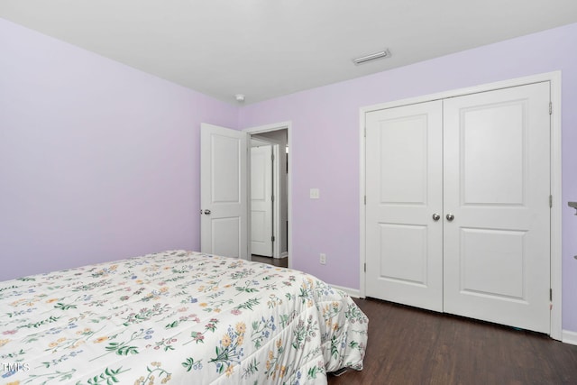 bedroom with a closet, dark wood-style flooring, visible vents, and baseboards