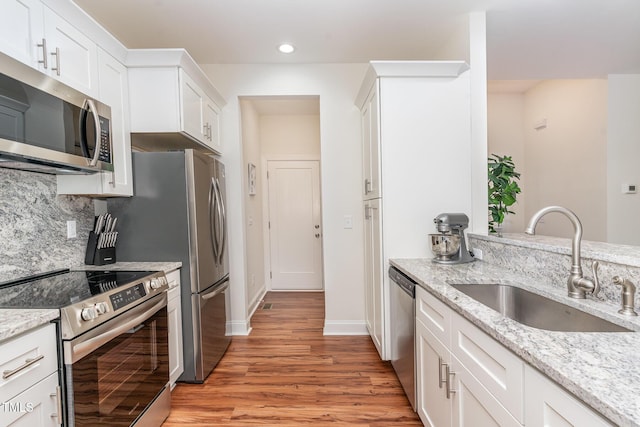 kitchen with stainless steel appliances, light stone counters, a sink, and white cabinetry