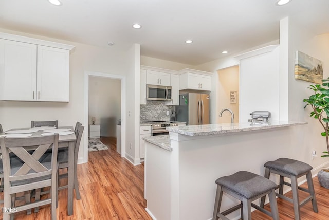 kitchen with white cabinets, a peninsula, light stone countertops, stainless steel appliances, and a kitchen bar