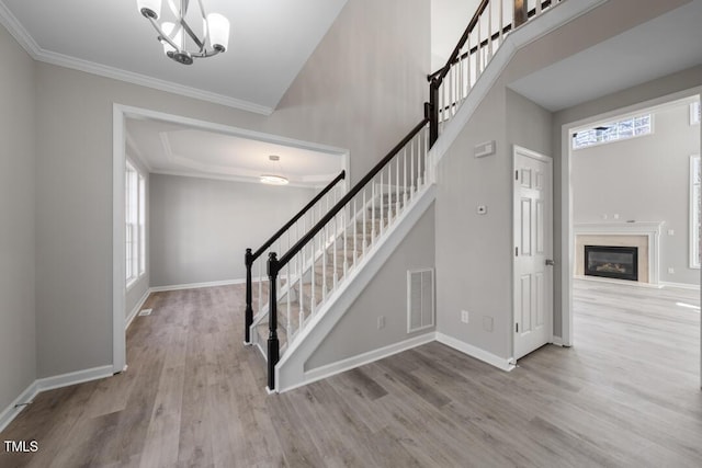 stairway featuring a towering ceiling, a fireplace, hardwood / wood-style flooring, a notable chandelier, and crown molding