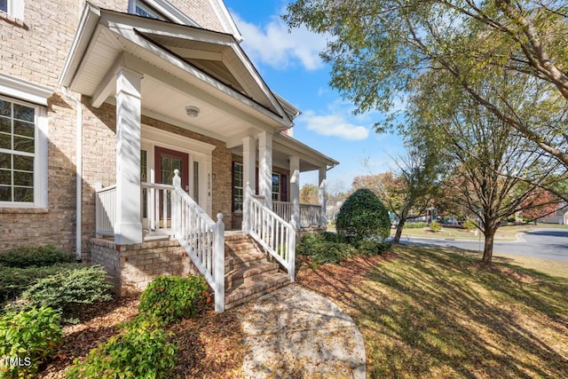 doorway to property featuring covered porch and brick siding