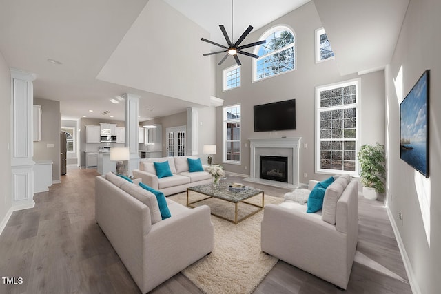 living room featuring a high end fireplace, baseboards, a ceiling fan, light wood-style floors, and ornate columns