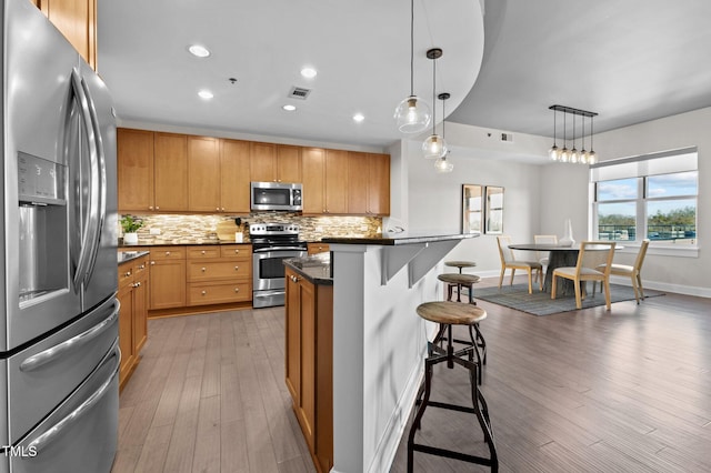 kitchen with a breakfast bar, dark countertops, backsplash, and appliances with stainless steel finishes