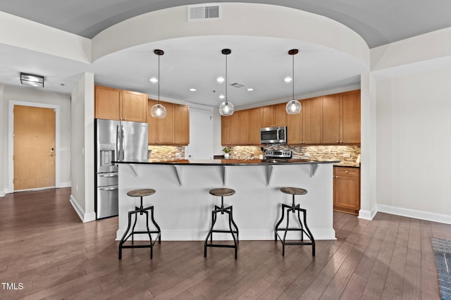 kitchen featuring visible vents, dark wood-type flooring, appliances with stainless steel finishes, dark countertops, and a kitchen breakfast bar