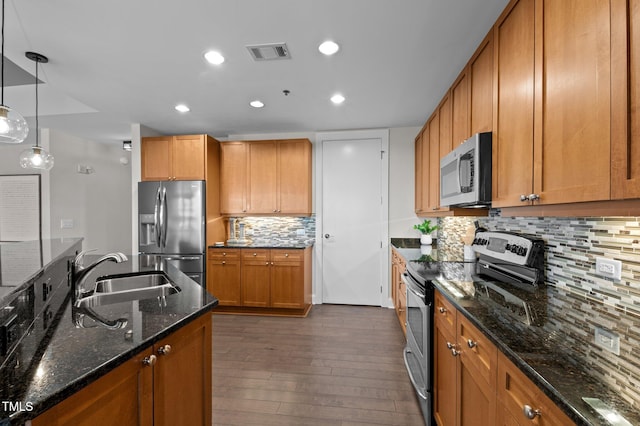 kitchen with brown cabinetry, visible vents, a sink, stainless steel appliances, and dark wood-type flooring