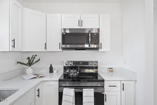 kitchen featuring appliances with stainless steel finishes, white cabinets, and light stone counters