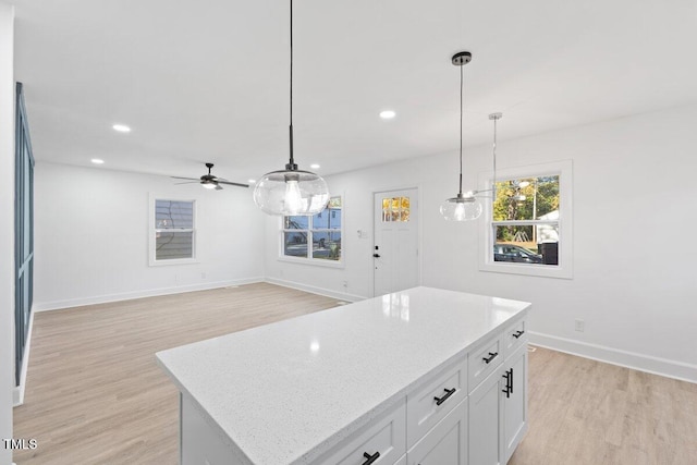 kitchen featuring decorative light fixtures, light hardwood / wood-style floors, a kitchen island, and white cabinets