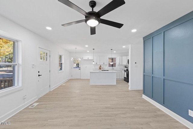 unfurnished living room with ceiling fan with notable chandelier and light hardwood / wood-style flooring