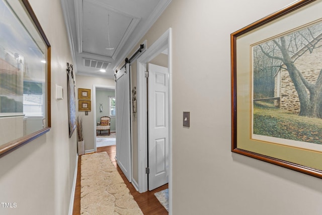 hallway with wood-type flooring, ornamental molding, and a barn door