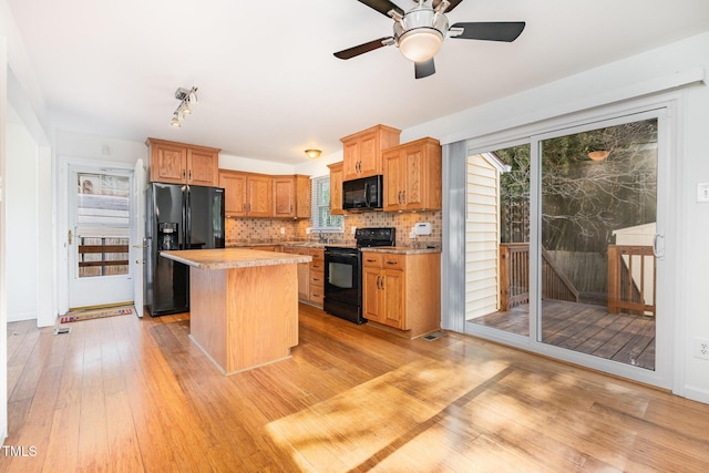 kitchen featuring ceiling fan, a center island, black appliances, decorative backsplash, and light wood-type flooring