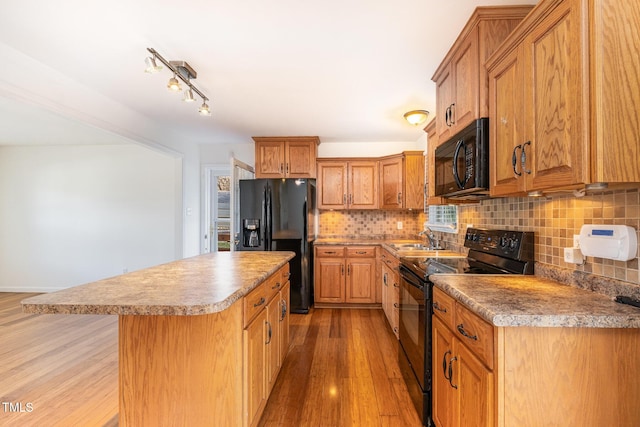 kitchen featuring sink, a center island, tasteful backsplash, light hardwood / wood-style floors, and black appliances