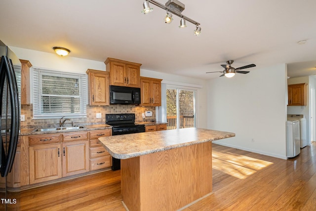 kitchen featuring sink, a center island, black appliances, washer and dryer, and decorative backsplash