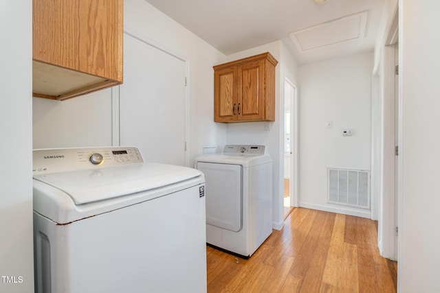 washroom featuring cabinets, washing machine and dryer, and light wood-type flooring