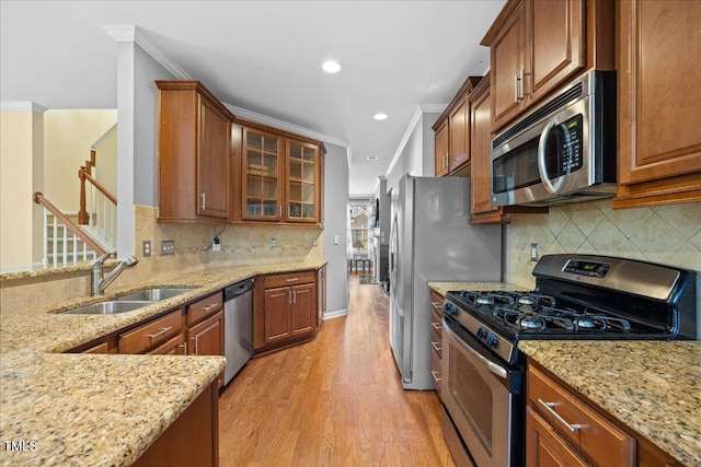 kitchen with appliances with stainless steel finishes, sink, light stone counters, crown molding, and light hardwood / wood-style flooring