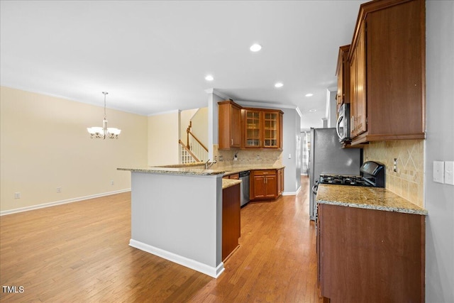 kitchen with light stone counters, hanging light fixtures, light wood-type flooring, kitchen peninsula, and stainless steel appliances