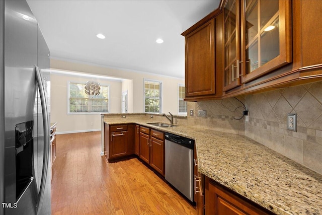 kitchen with sink, light stone counters, light hardwood / wood-style flooring, appliances with stainless steel finishes, and backsplash