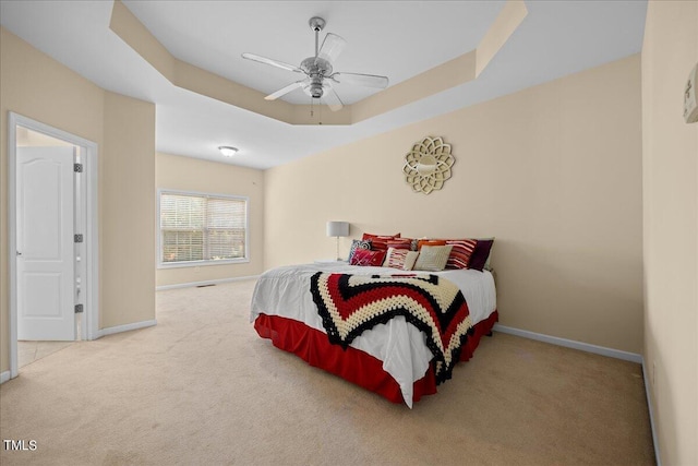 carpeted bedroom with ceiling fan and a tray ceiling